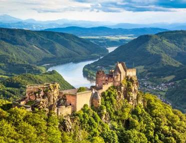 Forested landscape with Aggstein castle ruin and the Danube river at sunset in Wachau, Austria.