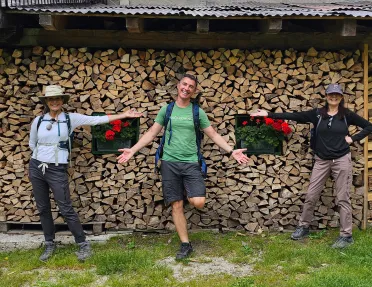 Three guests in front of wooden building, one in center, the other two gesturing to them.