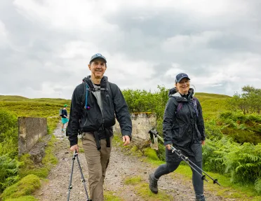 Man and woman holding hiking poles, walking on a dirt trial