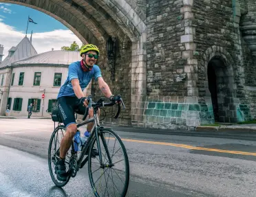 Man riding a bike on a road under a stone arc in a city