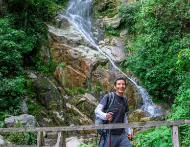 Man with a walking pole, walking across a wooden bridge with a small waterfall in the backgroun