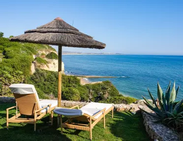 Two sun chairs below an umbrella on the coast of Portugal.