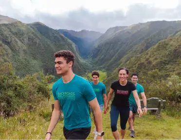 Group of people smiling while hiking up a grassy hill