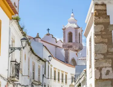 Historic street in the old town center of Lagos, Algarve, Portugal, looking toward the distinctive white bell tower of the Igreja de Santo António.